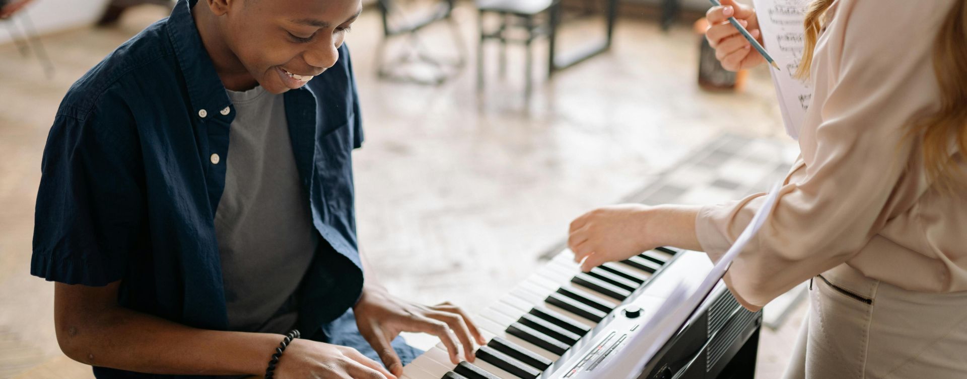 A young boy enjoying a piano lesson with a smiling teacher in a cozy indoor setting.