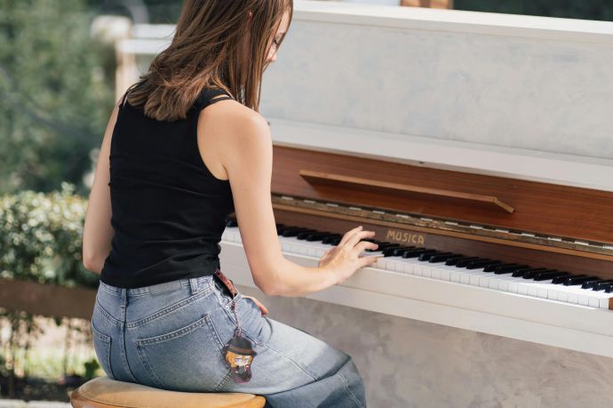 A young woman plays an upright piano outdoors on a sunny day, embracing music and relaxation.
