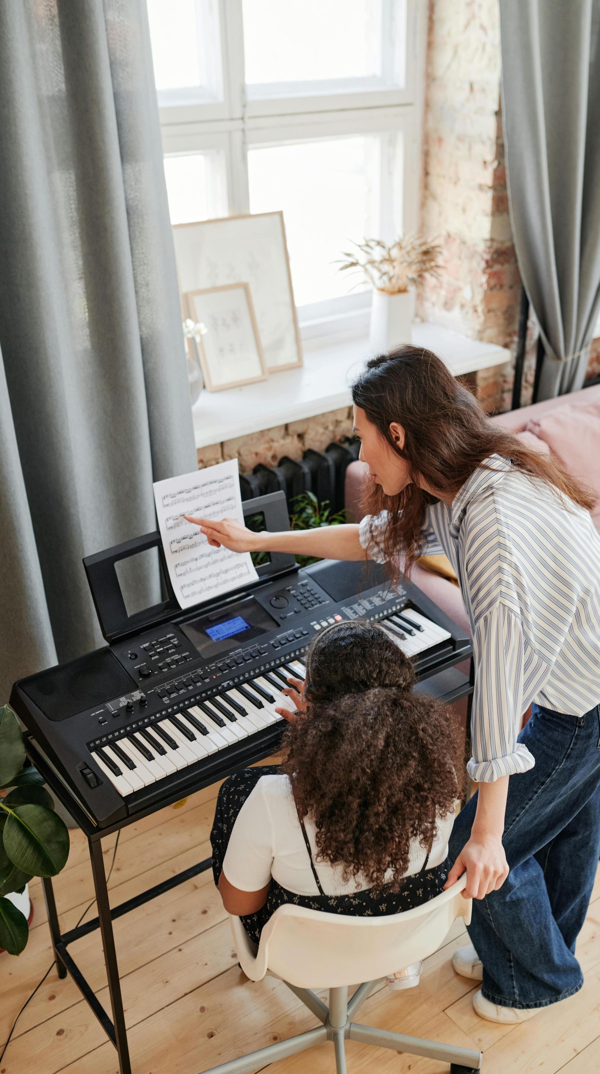 Woman teaching young girl piano lessons in a cozy living room setting.
