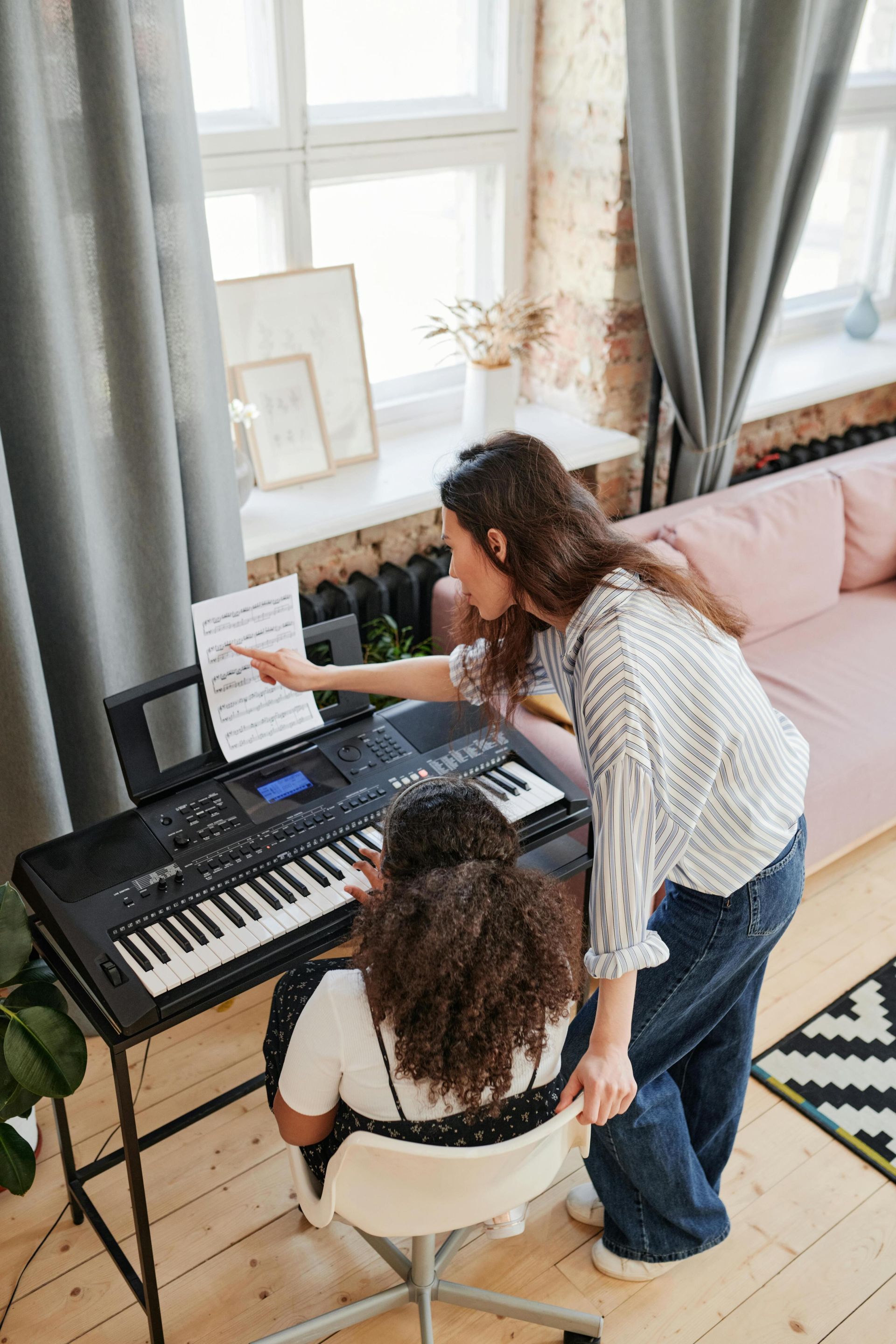 Woman teaching young girl piano lessons in a cozy living room setting.