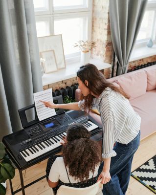 Woman teaching young girl piano lessons in a cozy living room setting.